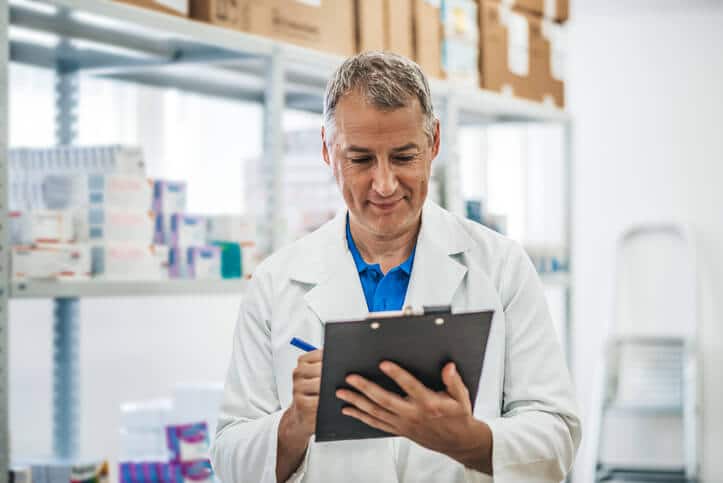 A male quality assurance associate holding a board at a factory after his pharmaceutical training